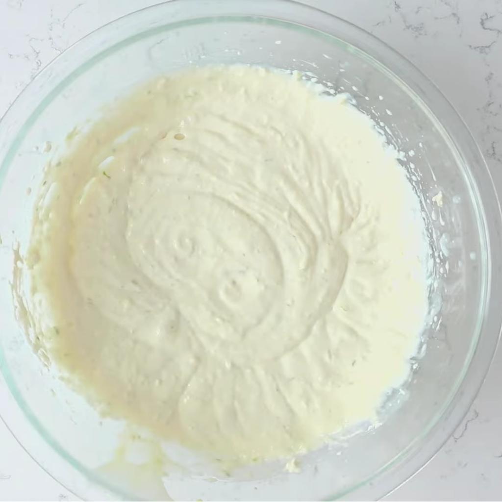 The fully mixed, creamy, and smooth no-bake key lime pie filling, showing swirls and flecks of lime zest, ready in a glass mixing bowl
