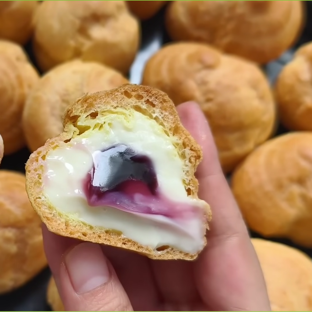 A close-up of a perfect cream puff, filled with white cream and a dollop of dark berry jam.