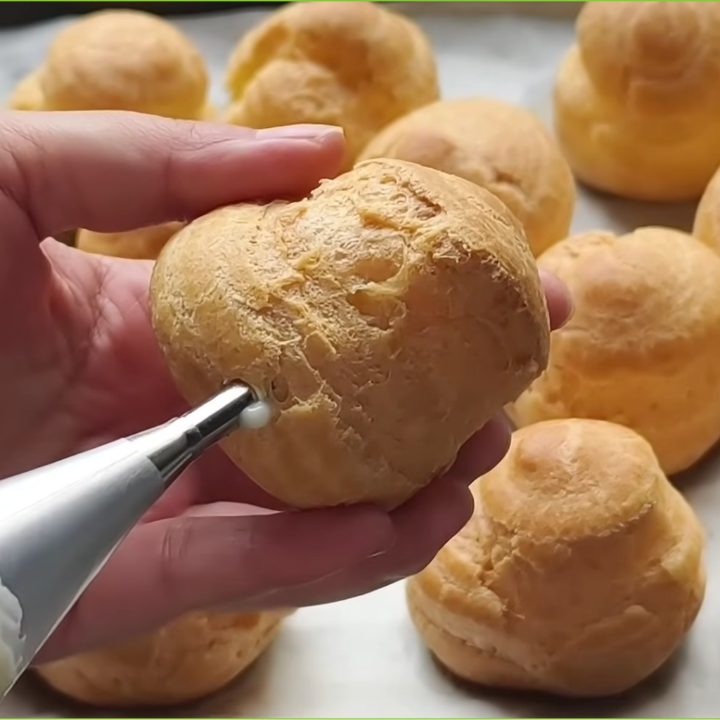 Perfectly baked golden brown cream puff shells resting on a parchment-lined baking sheet, ready to be filled.